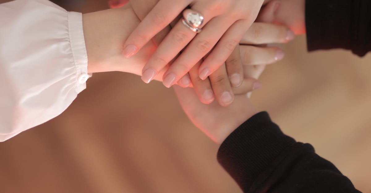 Top view of faceless friends in different clothes stacking hands together while standing on wooden floor indoor on sunny day