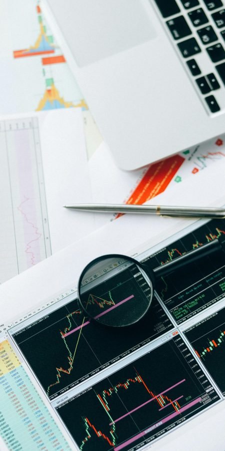 Magnifying glass and graphs depicting stock market data analysis on paper documents.